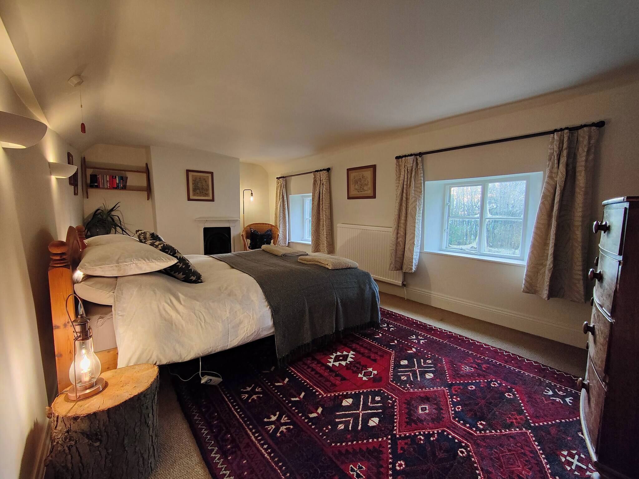 Ein Schlafzimmer mit zwei Betten, einem Kamin, einem Fenster mit Vorhängen, einer Heizung und einem traditionellen Teppich.