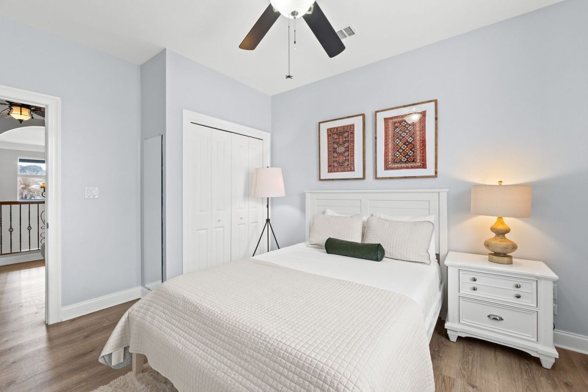 A bedroom with a bed, bedside tables, a ceiling fan, and framed artwork on the wall.
