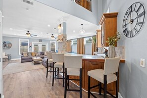 A spacious living area with a large sofa, a dining area with bar stools, and a kitchen with a wooden island. - Good Vibes: New Mgmt 2026, Relaxing Private Escape w/ Pool & Beach Service (Destin)