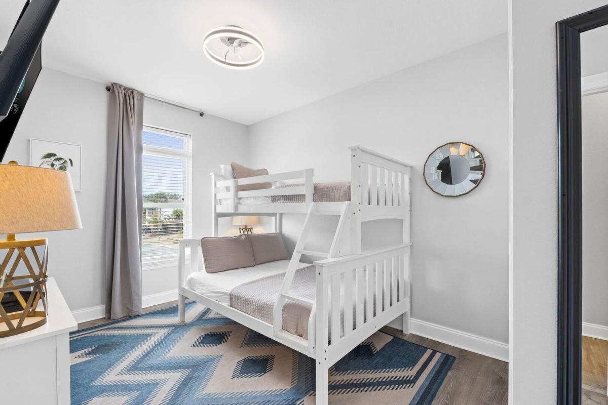 Ein Kinderzimmer mit Etagenbett, Lampe, Spiegel und einem gemusterten Teppich.