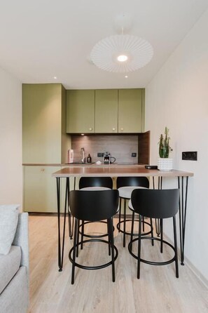 A modern kitchen with a wooden island, black bar stools, and a green cabinet. - Neostelia (Annecy)