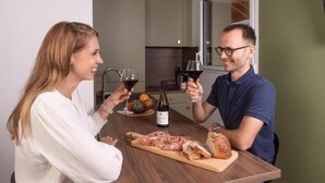 A dining table with a bottle of wine, a bowl of fruit, and a cutting board with sliced meat and bread. - Neostelia (Annecy)