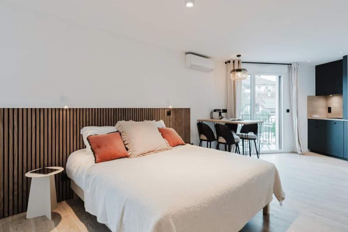 Moderni hotellihuone, jossa on sänky, yöpöytä ja ruokailualue tuoleineen.