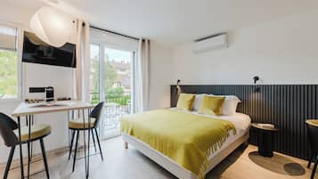 Une chambre moderne comprenant un lit, un bureau et des chaises, une télévision et une fenêtre donnant sur des immeubles.
