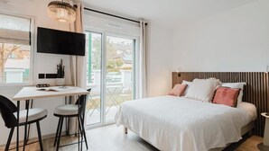 A modern bedroom with a bed, a desk, two chairs, a TV, and a window. - Neostelia (Annecy)