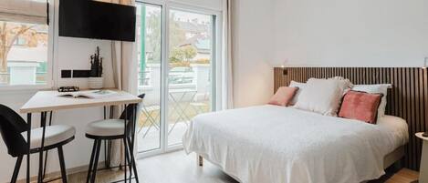 Un dormitorio moderno con una cama, un escritorio, dos sillas, un televisor y una ventana.