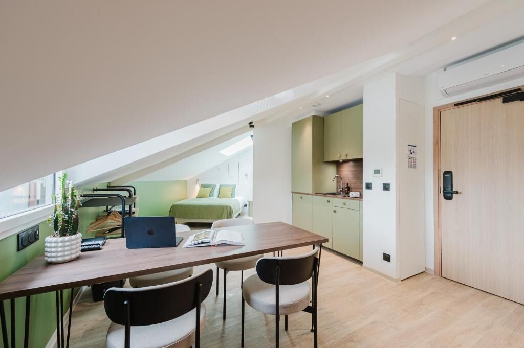 A modern room with a dining table, chairs, a laptop, and a bed in the background.