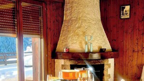A wooden dining area with a stone fireplace, a table set for four, and a view of a snowy landscape through the glass door. - Charming Vintage Flat Near Spa & Slopes (Leytron)