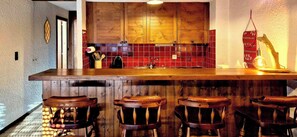 Eine Küche mit Holzausstattung, rotem Fliesenrückwand und einer Bar mit Hockern.