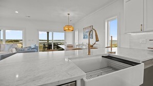 A modern kitchen with a large island, white cabinetry, and a view of the outdoors. - The Jolly Gator #212 Resort Pool, Private Hot Tub, Elevator, Game Room (Surf City)