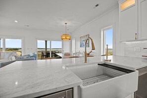 A modern kitchen with a large island, white cabinetry, and a view of the outdoors. - The Jolly Gator #212 Resort Pool, Private Hot Tub, Elevator, Game Room (Surf City)