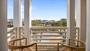 A balcony with white railings and wooden chairs, overlooking a residential area with houses and trees. - The Jolly Gator #212 Resort Pool, Private Hot Tub, Elevator, Game Room (Surf City)