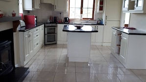 A spacious kitchen with white cabinets, a central island, a stove, and a red ceiling light. - Ballyferriter Dingle Seaside Beautiful House (Ballyferriter)