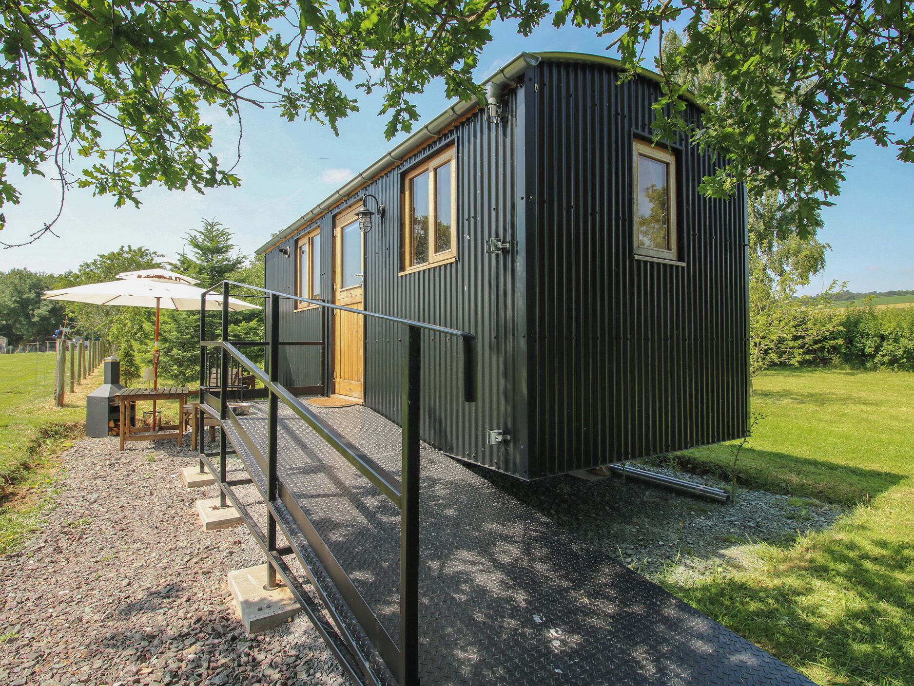 Une petite cabane à un seul étage, au revêtement extérieur en métal, dotée d’un petit porche et d’un chemin de gravier menant à l’entrée.