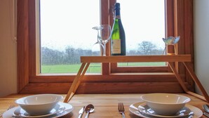 A dining setup with two bowls, a wine bottle, and a glass on a wooden table by a window. - Daves Place (Much Wenlock)