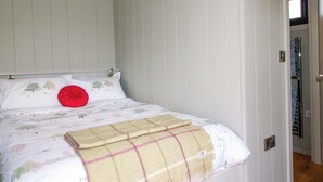 Un dormitorio con cama, paredes blancas, una puerta y una ventana.