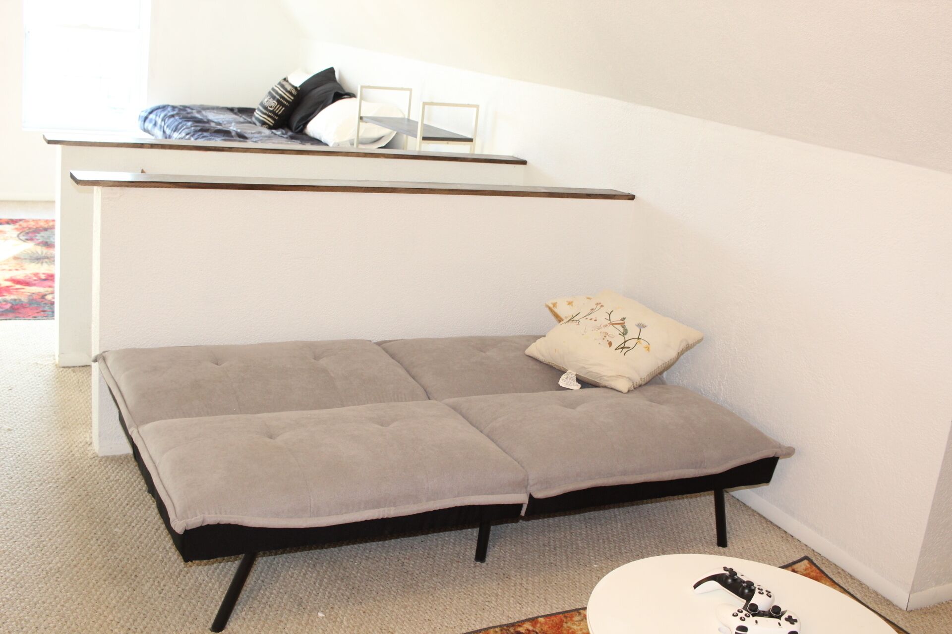 Een kleine, moderne kamer met een grijze slaapbank, een klein tafeltje met een wit oppervlak en een zwarte stoel.
