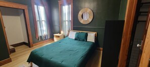 Un dormitorio con una cama, una mesita de noche, un espejo y una ventana con cortinas.