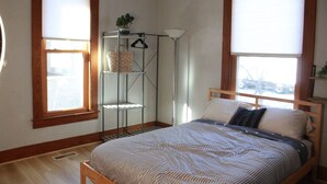 Un dormitorio con una cama de madera, un estante metálico y una ventana con persianas.