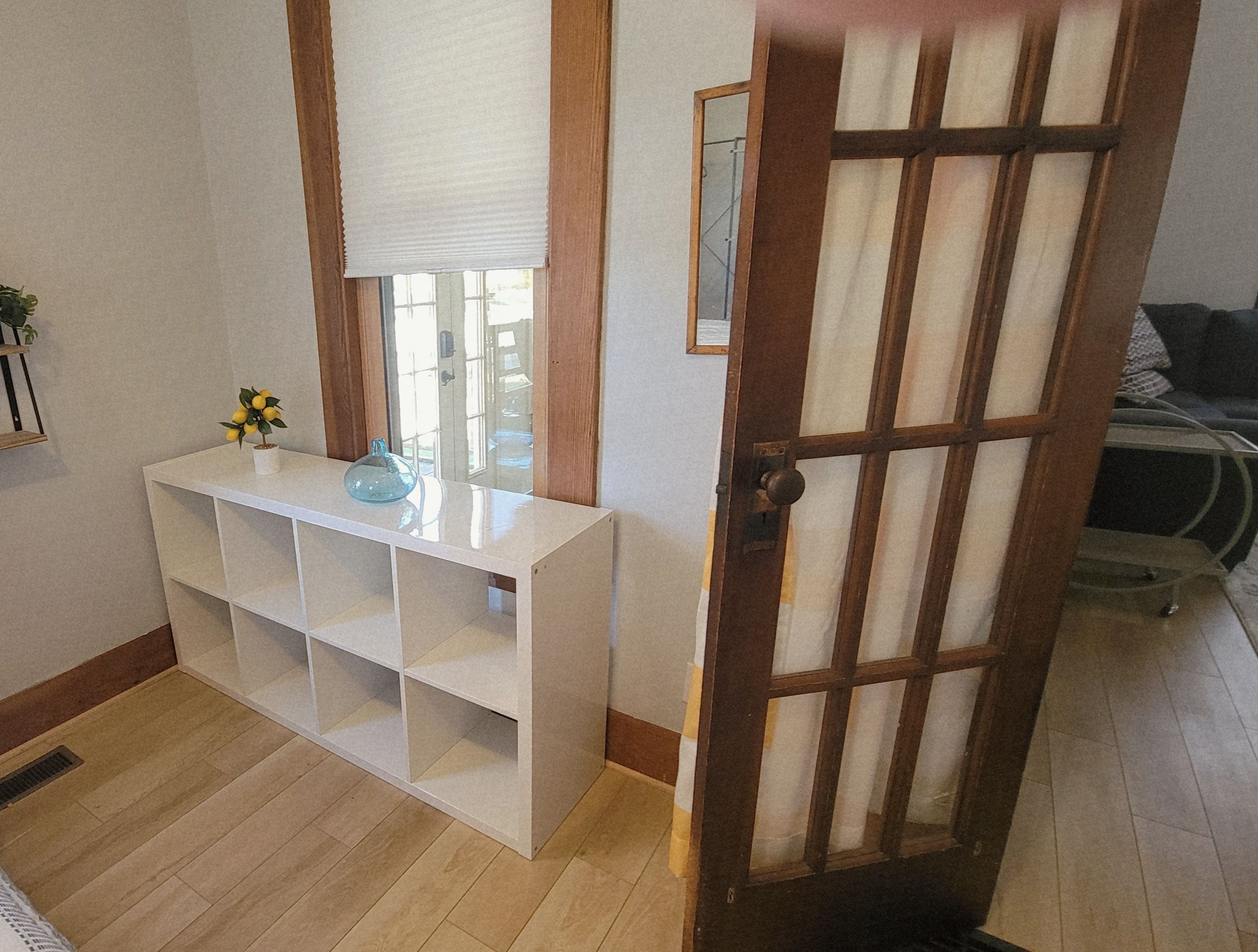 A room with a white console table, a door with a wooden frame, and a window with a blind.