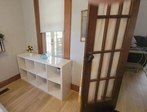 Una habitación con una consola blanca, una puerta de madera y una ventana con persiana.