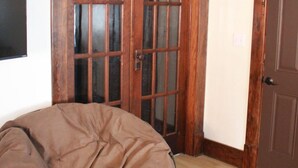 Una habitación con piso de madera, un sillón redondo con cojín marrón y dos puertas de madera con paneles de vidrio.