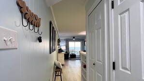 A hallway with a wooden leaf-shaped wall decoration, a small stool, and a patterned rug. - Isle Be Back - Oceanfront Ocean Isle (Ocean Isle Beach)