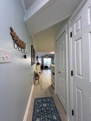 A hallway with a wooden leaf-shaped wall decoration, a small stool, and a patterned rug. - Isle Be Back - Oceanfront Ocean Isle (Ocean Isle Beach)