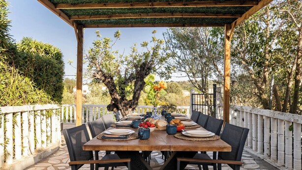En uteservering med en träpergola, stenplattor på golvet och ett bord med plats för sex personer, tillsammans med stolar.