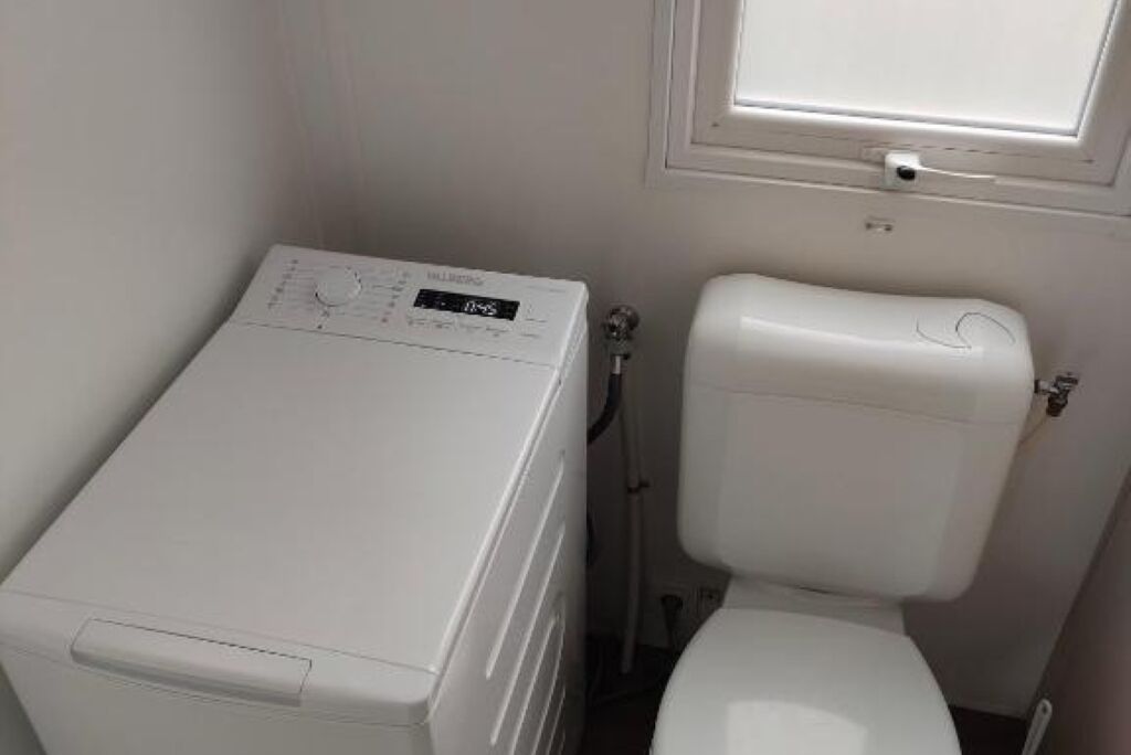 Een kleine badkamer met een witte wasmachine en toilet.