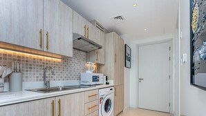 A compact kitchen with a washing machine, a microwave, and a sink. - Sea View, Stylish upgraded studio in Seven Palm (Dubai Emirate)