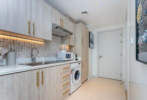 A compact kitchen with a washing machine, a microwave, and a sink. - Sea View, Stylish upgraded studio in Seven Palm (Dubai Emirate)