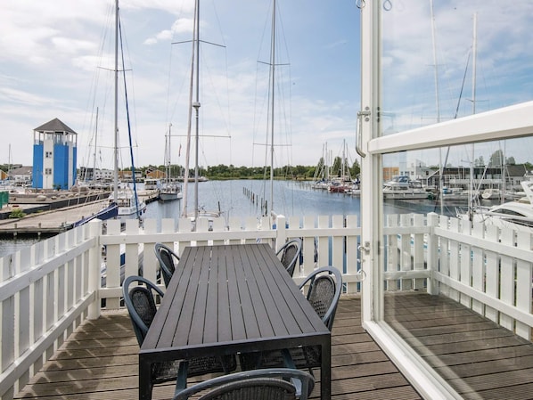 Una terraza de madera con una mesa y sillas, con vistas a un puerto deportivo con varios veleros amarrados.