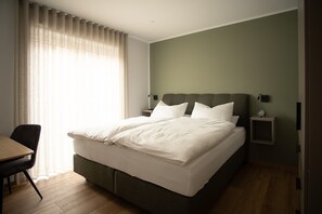 Habitación de hotel con cama, escritorio, silla, mesita de noche y ventana con cortinas.