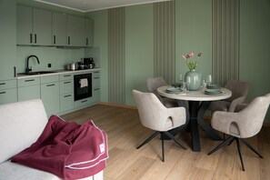 Una cocina moderna con armarios verde claro, un rincón comedor con dos sillas, una mesa redonda y un florero con flores.