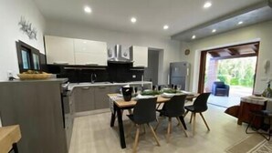A modern kitchen with white cabinets, a dining area with a table and chairs, and a view of the outdoors through a glass door. - Villa Lavinia - Alghero (Alghero)