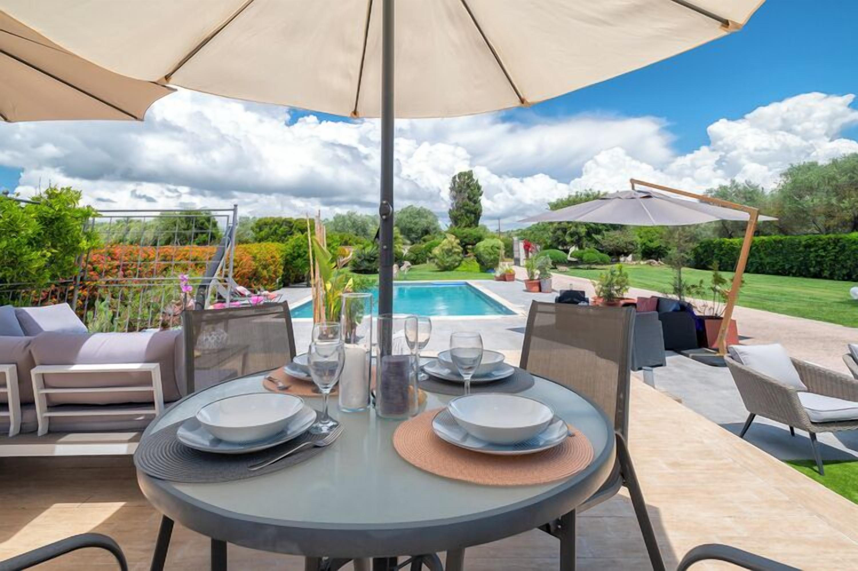 An outdoor dining area with a table set for two, surrounded by chairs and a large umbrella.