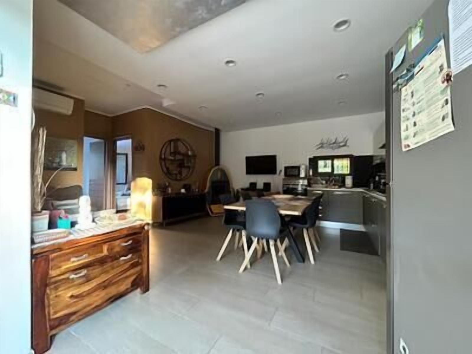 A modern kitchen with a dining area, featuring a wooden cabinet, a dining table with chairs, and a refrigerator with a paper on it.