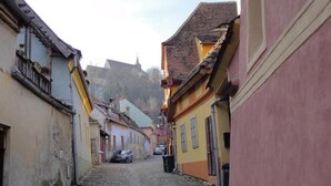 Eine enge Kopfsteinpflasterstraße, gesäumt von bunten Häusern, mit einem Kirchturm in der Ferne und geparkten Autos.