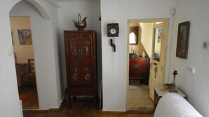Ein Zimmer mit Holzboden, einem Bett mit kariertem Überwurf, einem Holzschrank, einer Wanduhr und einer Tür zu einem weiteren Raum.