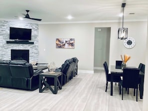 A modern living room with a black leather sofa, a fireplace, a flat-screen TV, and a dining area with a table and chairs. - Luxe Lakehouse-kemah  For 8 (Kemah)
