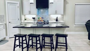 Una cocina moderna con armarios blancos, encimera negra y tres taburetes negros.