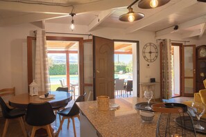 A kitchen with a dining area, a clock on the wall, and a door leading to a patio. - Villa Serena - Alghero (Alghero)