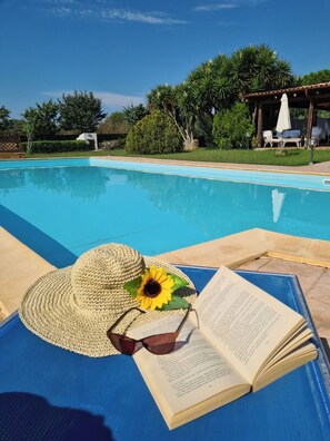 A poolside area with a sun lounger, a straw hat, sunglasses, and a book.