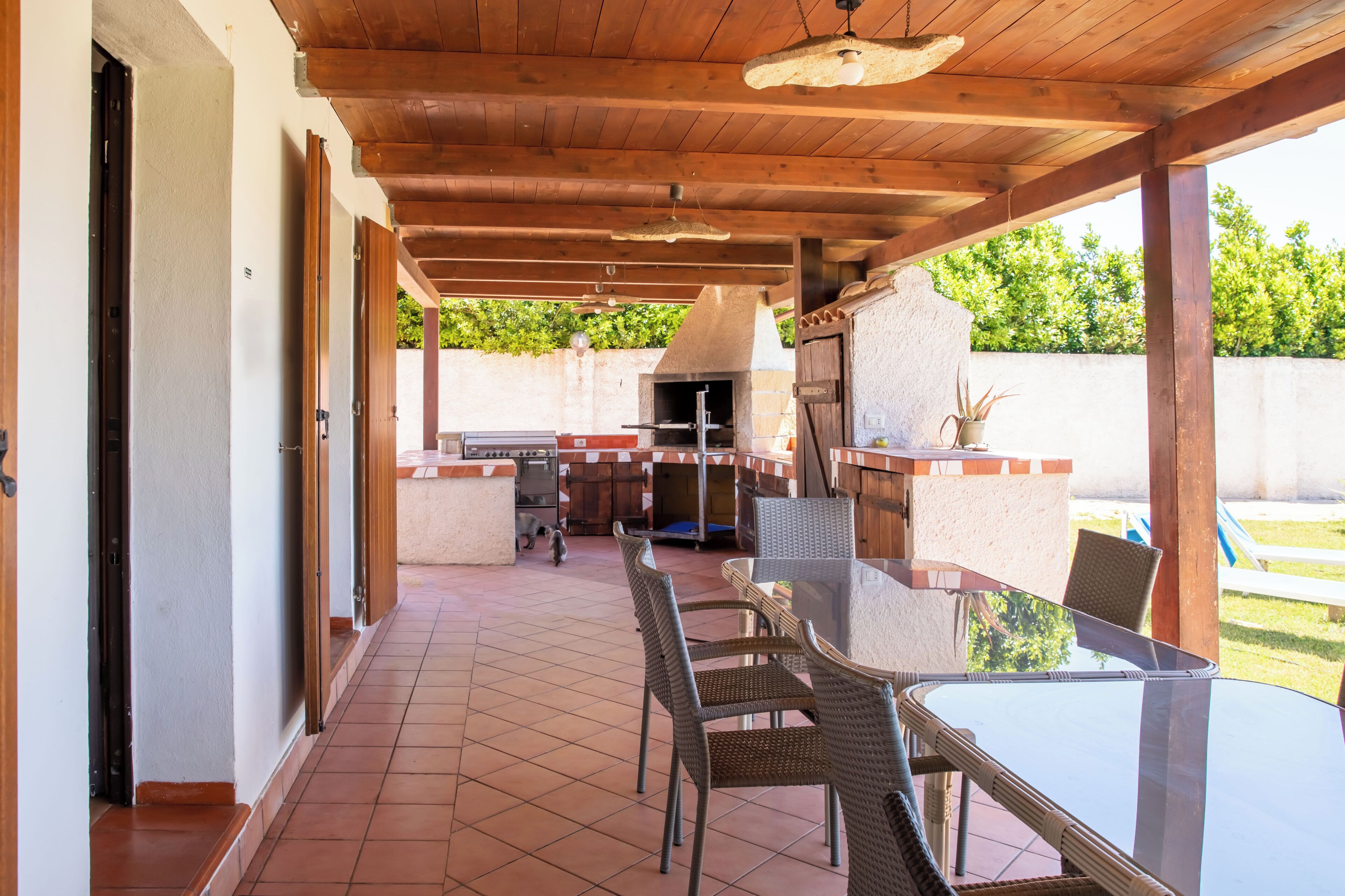 An outdoor patio with a glass table, wicker chairs, a grill, and a tiled floor.