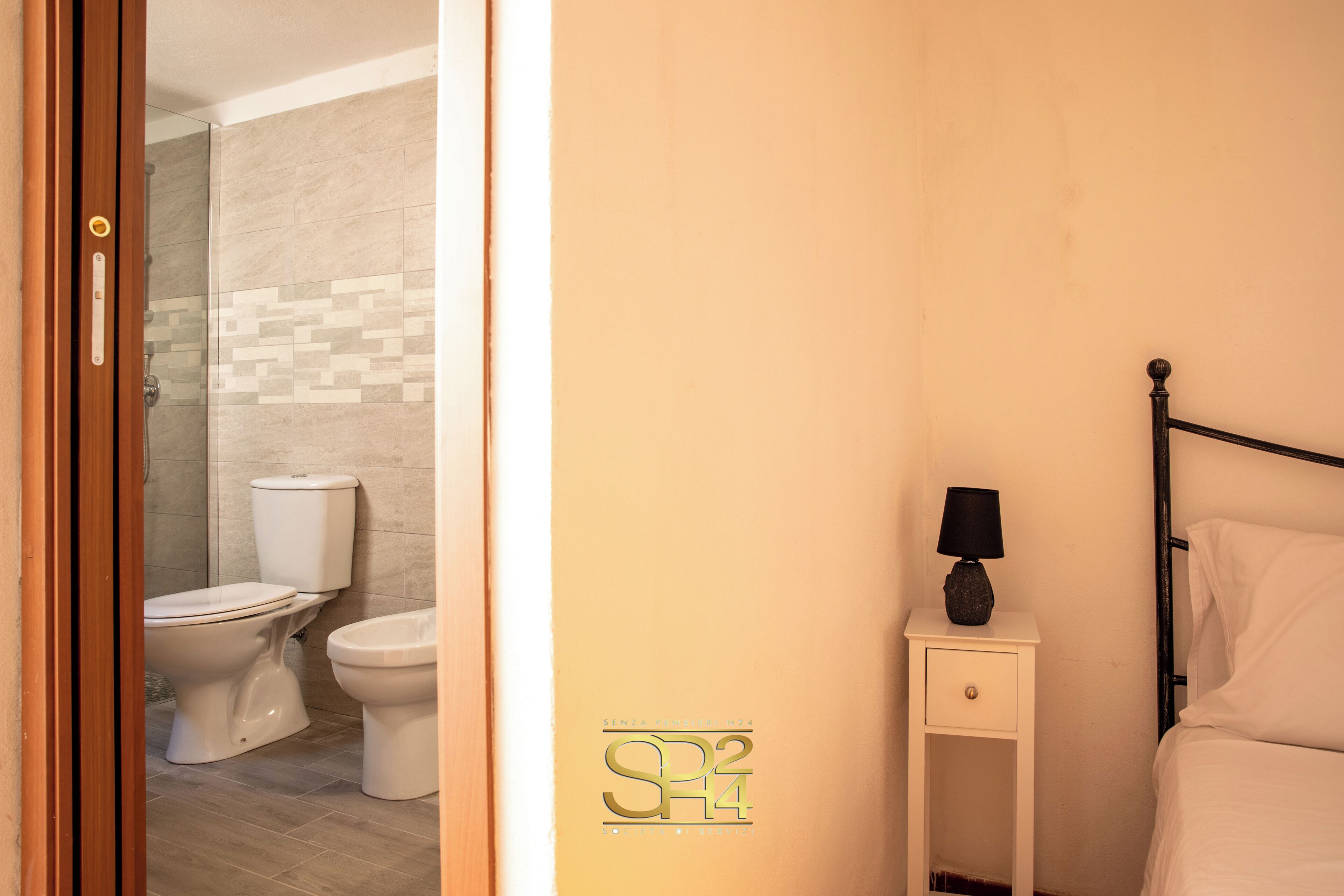 Un baño con inodoro, ducha y cama con mesita de noche.
