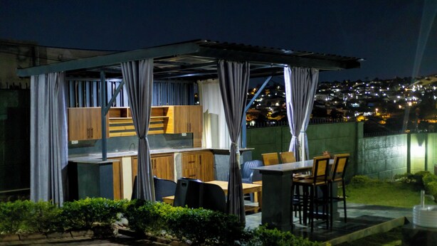 A covered outdoor dining area with wooden furniture and a view of a cityscape at night. - Fabulous 4BDR villa with a jacuzzi in exciting Kigali Kimironko for your getaway (Kigali)