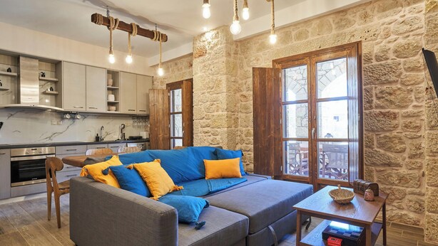 A cozy living area with a sofa, a wooden table, and a kitchen in the background. - Porto Santo Mani 1st Apartment (Mani)