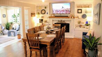 A dining area with a wooden table set for six, flanked by chairs, a fireplace, and a television mounted above.