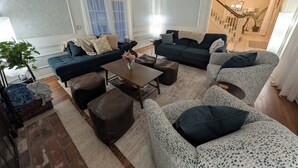 A living room with a dark blue sofa, a patterned armchair, a coffee table, and a brown ottoman.
